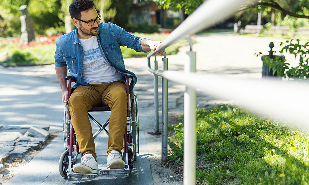 A young man in a wheelchair uses a handrail to go up a ramp.