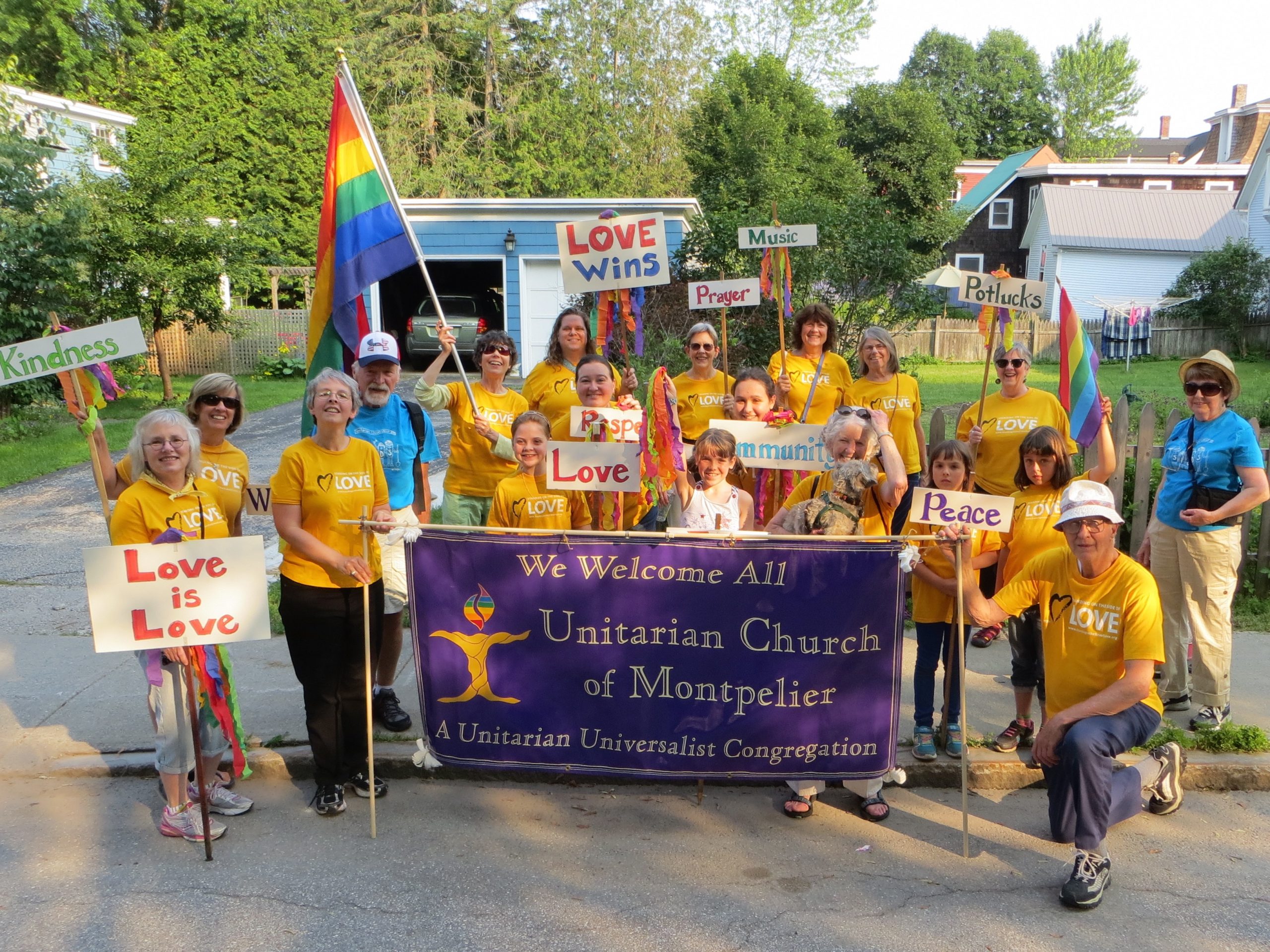 A group of people from the Unitarian Church are gathered together with flags and rainbows and a large banner about their church.