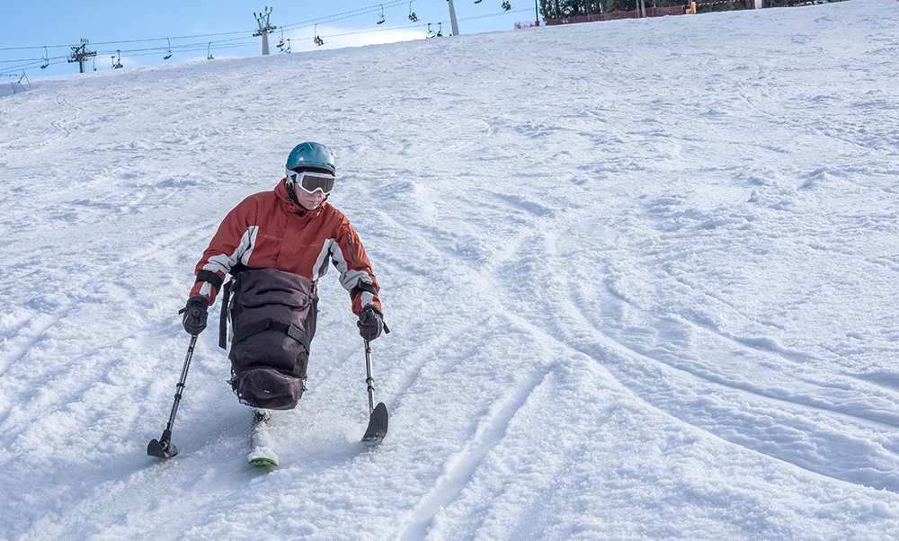 A man is sit-skiing down a mountain at a ski resort.