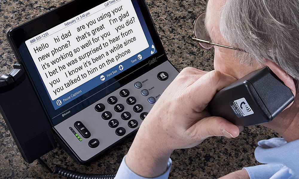 A close-up of a captioning phone while an elderly man uses it