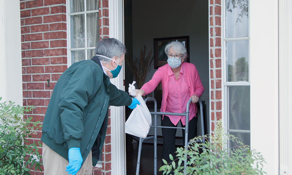An older man is delivering a meal to an elderly woman at her front door.