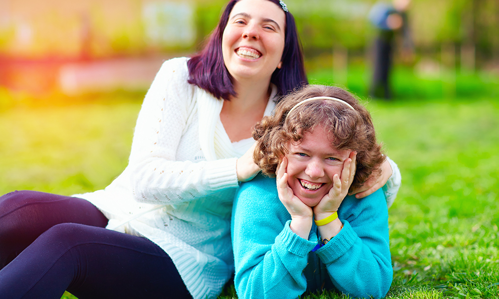 Two teenage girls are laughing and playing in the grass on a sunny day