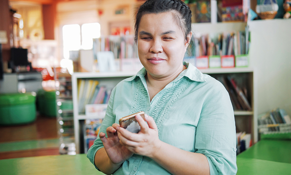 A young woman with impaired vision sits in a colorful home, she is using the touchpad on her cell phone